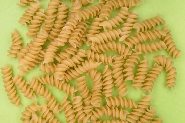 Uncooked rotini pasta spirals scattered on a bright green surface, ideal for culinary themes.