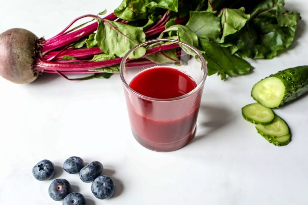 Glass of fresh beetroot juice with cucumbers and blueberries on a white background.
