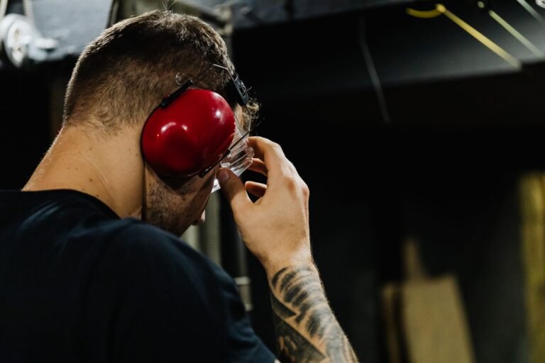 Close-up of a man adjusting safety glasses with red earmuffs in an indoor setting.