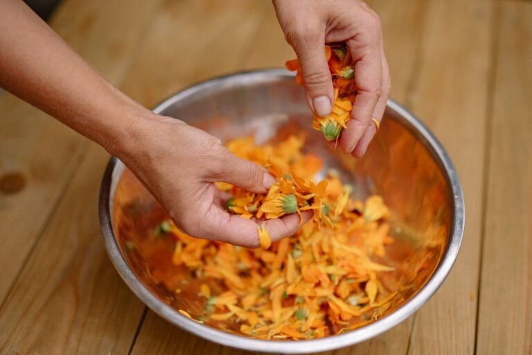 Close-up of hands sorting vibrant orange flower petals in a metal bowl, emphasizing natural textures.