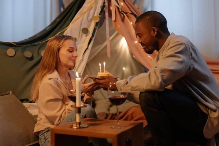 A couple celebrating a birthday indoors with candles and wine, creating a romantic atmosphere.