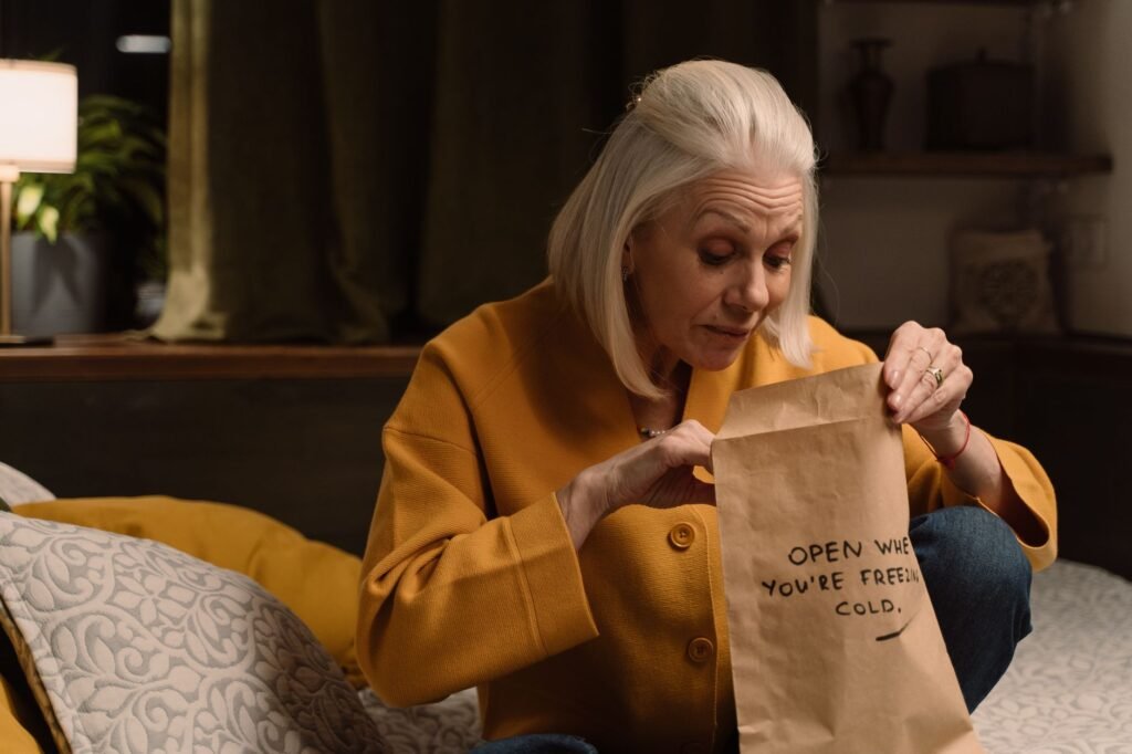 Senior woman in yellow unpacking a mysterious gift in a cozy bedroom setting.