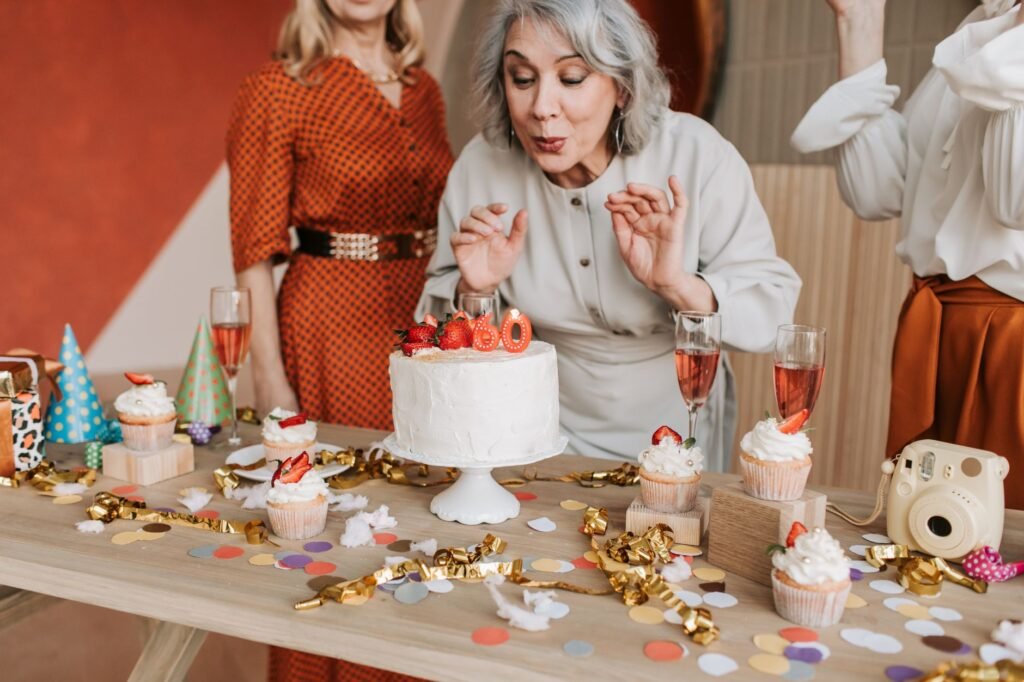 Joyful senior woman blowing out candles on her 60th birthday cake surrounded by friends.