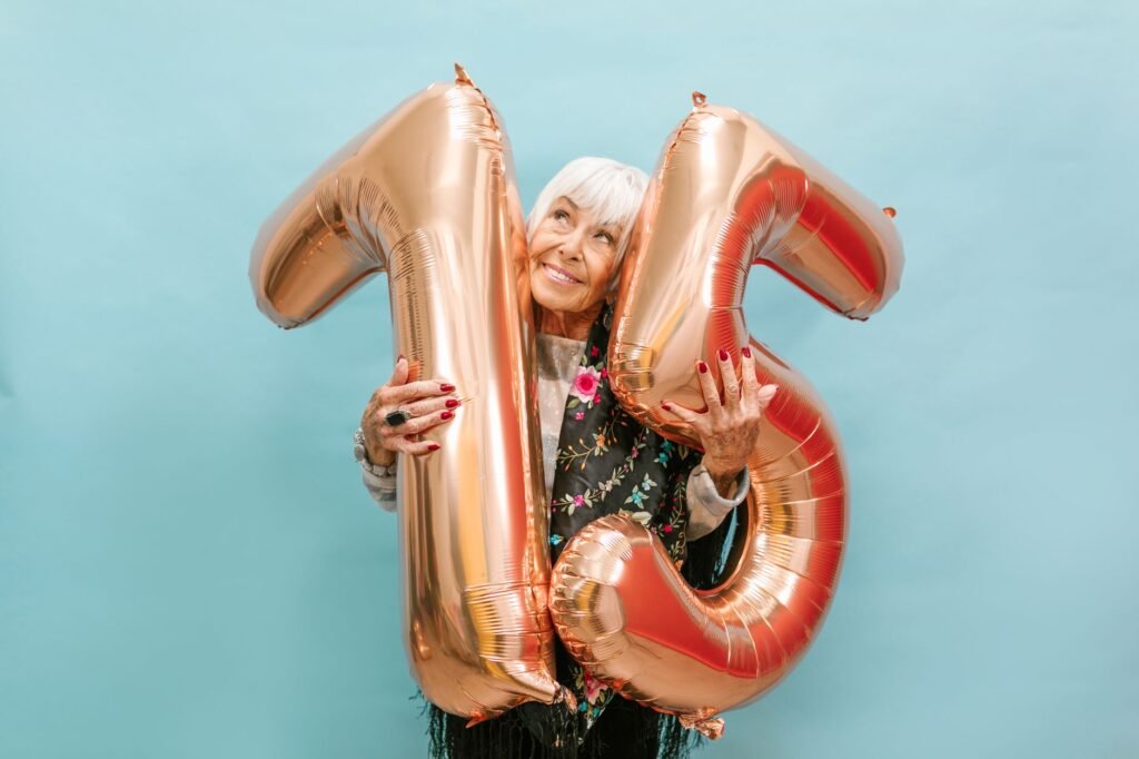 Elderly woman joyfully celebrating her 75th birthday with balloon numbers and a bright blue backdrop.