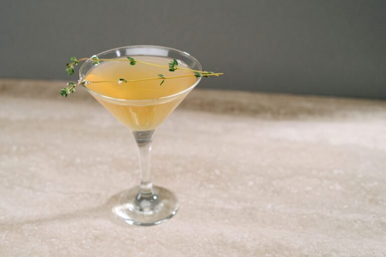 A stylish yellow cocktail garnished with fresh herbs in a martini glass against a neutral backdrop.
