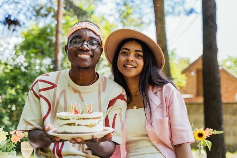 Two adults celebrating a birthday outdoors with a cake adorned with candles, smiling and happy.
